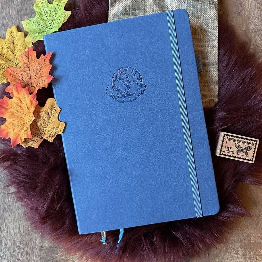 Dotted Notebook B5 160 GSM - Globe frÄn Paper24. BlÄ anteckningsbok med motiv med en hand som hÄller i en jordglob. Bredvid Àr det lönnlöv. - Tidformera