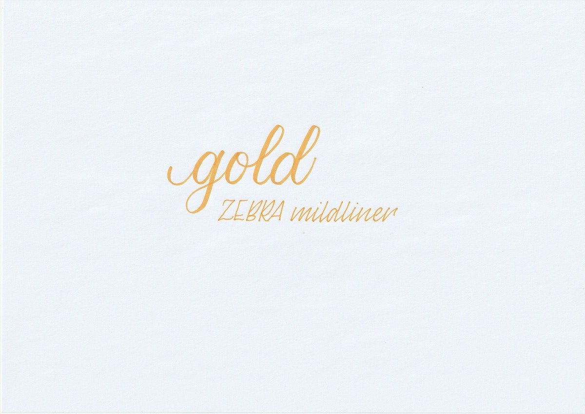 Handskriven text med orden "gold" och "ZEBRA mildliner" i guld färg, skriven med Zebra Mildliner Brush Pen i färgen Gold.