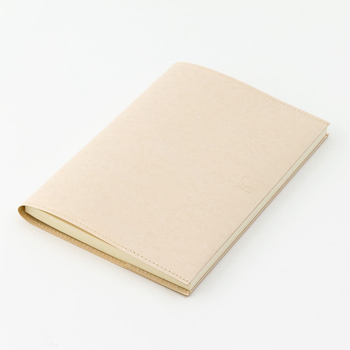 Notebook Cover A5 - Paper från Midori. Skrivbok ligger på ett vitt bord. Skrivboken har creamfärgat bokomslag på. Tidformera