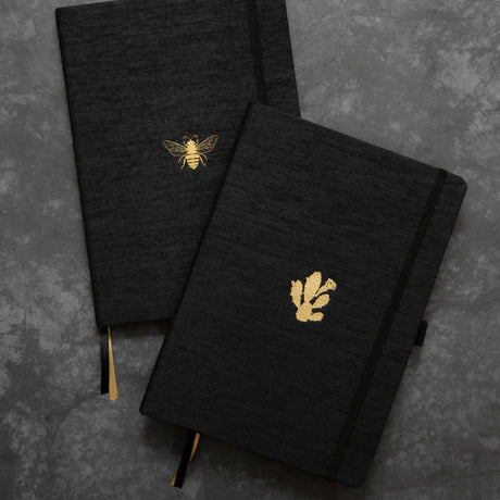 Anteckningsbok B5 PRO Cactus Dotted. Två anteckningböcker i samma serie - B5 PRO. Båda är svarta och har guldfärgade motiv mitt på pärmen. Ena motivet ä ett bi, den andra en kaktus. Från Dingbats* - Tidformera