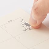 Kalenderstickers Djurtema - Birds från  Midori. Ett finger fäster ett  klistermärke med en fågel i en kalender. Tidformera