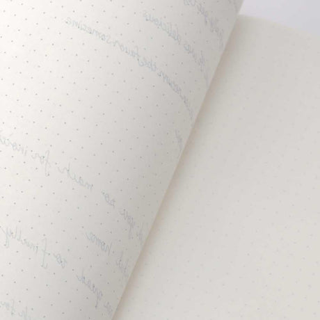 TomoeRiver Notebook softcover - A5 - Dot Grid från Sakae TP. En uppslagen skrivbok med en inlaga med prickar. Baksidan av ett ark och skrift skymtar genom från andra sidan. 